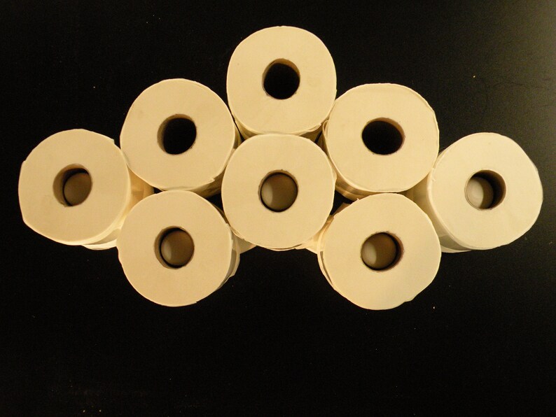 May include: A group of eight white toilet paper rolls arranged in a semi-circle shape on a black surface.