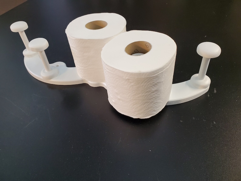 May include: White toilet paper holder with two rolls of toilet paper. The holder has four white knobs on the sides.
