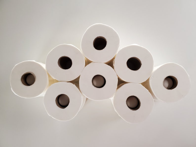 May include: A close-up of eight white toilet paper rolls stacked in a pyramid shape.