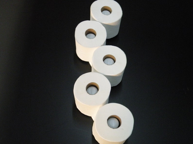 May include: Five white toilet paper rolls stacked on top of each other on a black surface.