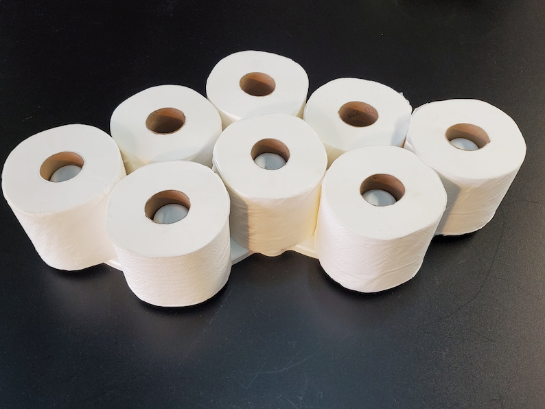 May include: Eight white toilet paper rolls arranged in a circle on a black surface.