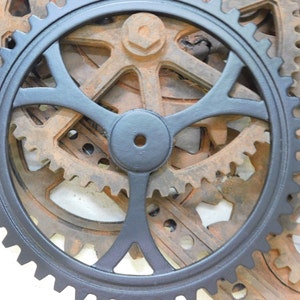 May include: A set of black and brown metal gears, with the largest gear painted black and featuring a four-spoke design. The gears are interlocked and create a decorative wall art piece.