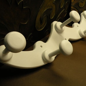 May include: White wooden coat rack with a curved design and multiple hooks. The rack is painted white and has a smooth finish.