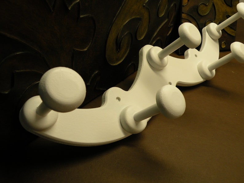 May include: White wooden coat rack with a curved design and multiple hooks. The rack is painted white and has a smooth finish.