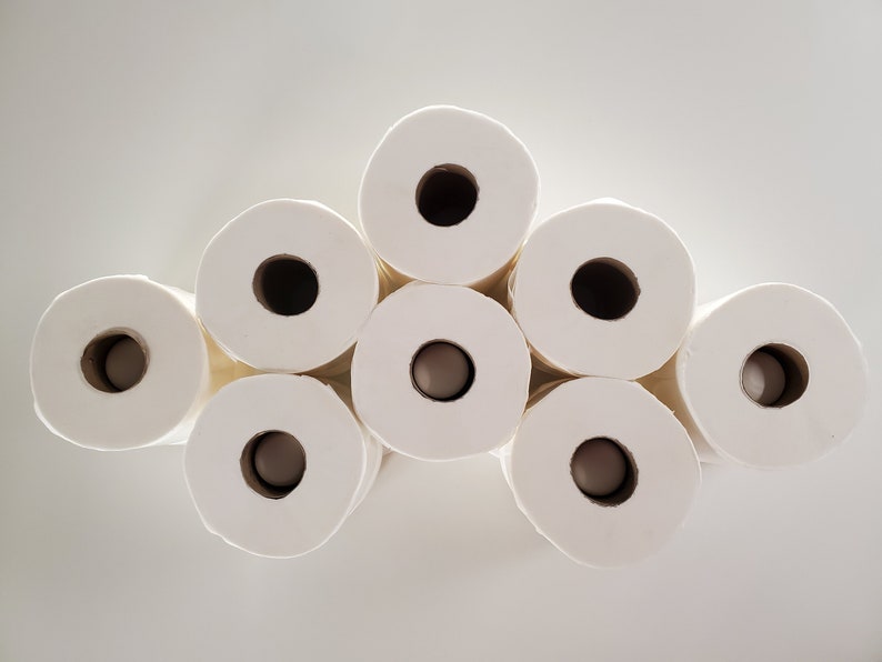 May include: A stack of eight white toilet paper rolls arranged in a pyramid shape.