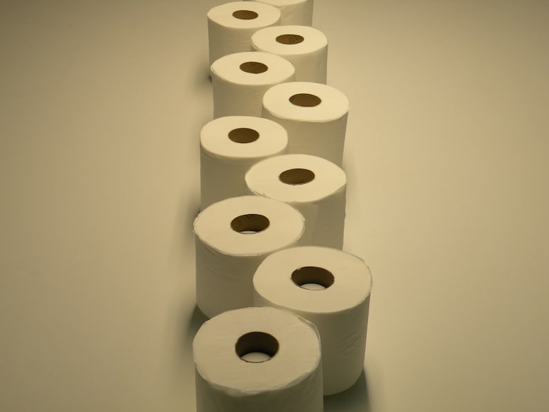 May include: A row of white toilet paper rolls stacked vertically on a white surface.