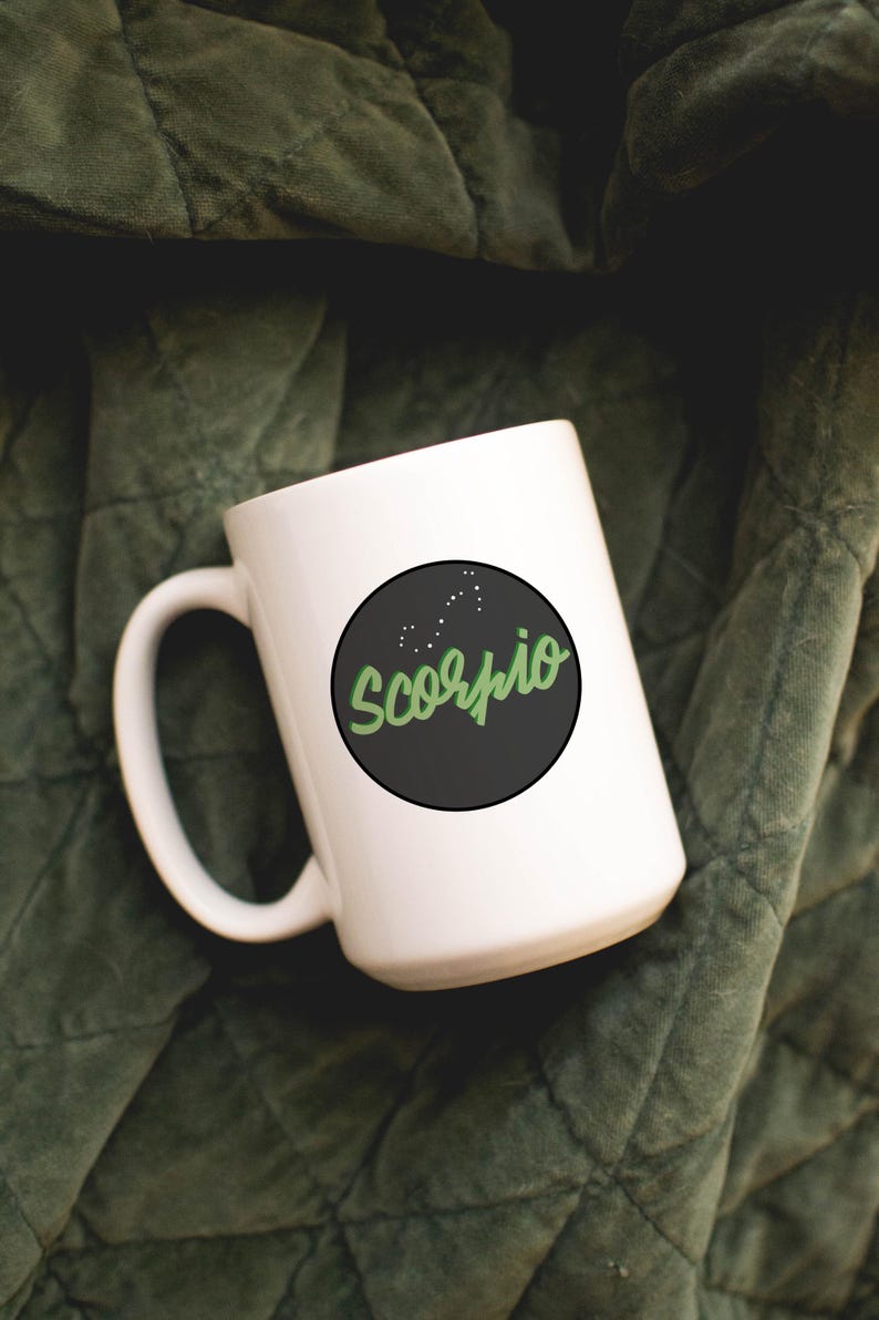 May include: White ceramic mug with a black circle featuring the word "Scorpio" in green script, along with a constellation design. The mug is set against a dark green, textured background.