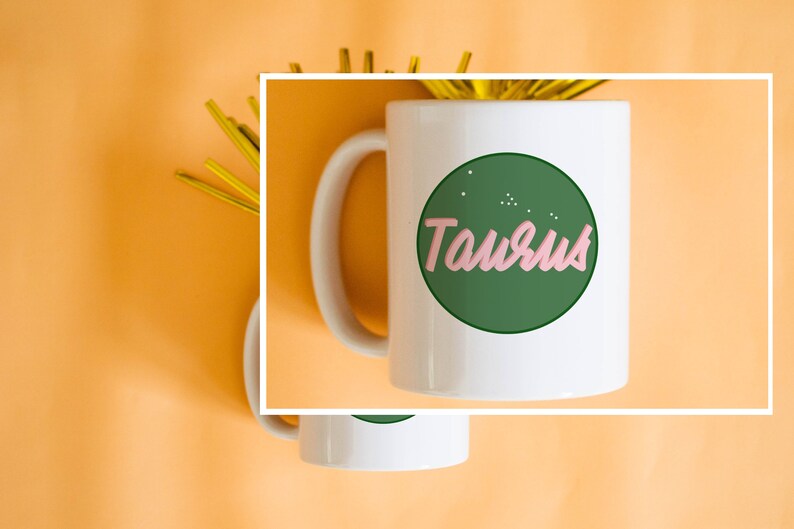 May include: White ceramic mug featuring the word "Taurus" in pink script within a green circle, with small white dots. The mug has a white handle and is set against an orange background with gold decorative elements.