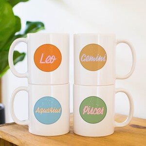 Four 11oz white coffee mugs with zodiac signs. Each zodiac sign has a circle with the zodiac color for each sign. Constellation stars are above each text in the circle.
