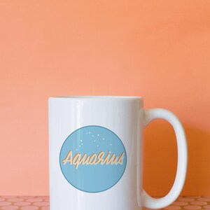 May include: White ceramic mug with a blue circle featuring the word "Aquarius" in a light orange script. The mug has a large handle and is set against an orange background.