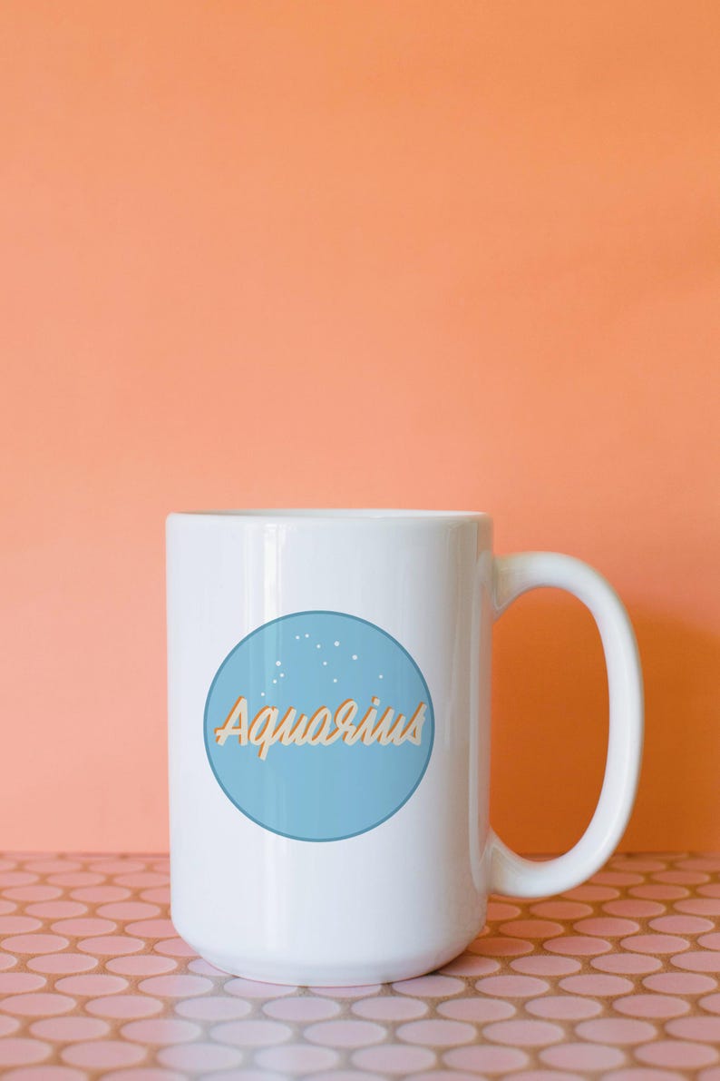 May include: White ceramic mug with a blue circle featuring the word "Aquarius" in a light orange script. The mug has a large handle and is set against an orange background.