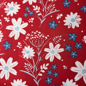 May include: A close-up of a red fabric with a floral pattern. The design features white and blue flowers, along with white and light blue stems and leaves. The flowers are in various sizes and shapes, creating a visually appealing design.