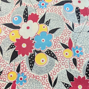 May include: A floral fabric pattern featuring a repeating design of stylized flowers and circular elements. The flowers are in shades of red, white, blue, and yellow, with black leaf accents, set against a cream background.