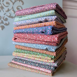 May include: A tall stack of folded fabric squares, each featuring a distinct small-scale floral pattern in a variety of colors including purple, light blue, yellow, dark blue, red, green, black, and tan, arranged in a vertical pile.