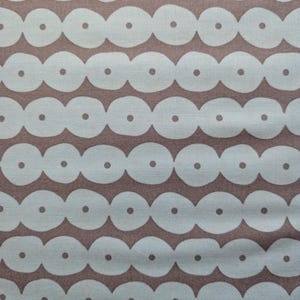 May include: Close-up of a fabric with a repeating pattern of white, oval shapes with a small dot in the center, set against a muted brown background. The design creates a chain-like effect, suitable for various textile applications.