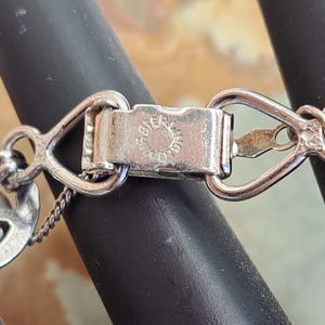 Op de afbeelding: Zilveren sluiting met een ronde bedel met een decoratief ontwerp. De sluiting is gemarkeerd met "925 Sterling".
