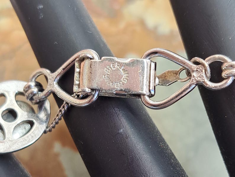 Op de afbeelding: Zilveren sluiting met een ronde bedel met een decoratief ontwerp. De sluiting is gemarkeerd met "925 Sterling".