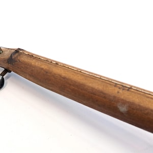 May include: A wooden musical instrument with a single string and a black tuning peg. The instrument is made of light brown wood and has a simple design.