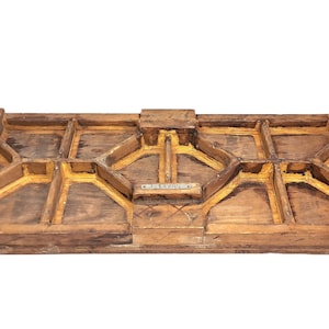May include: A long, rectangular wooden object with a geometric design. The object is primarily brown with yellow accents in the recessed areas. It features a series of interconnected shapes and compartments, suggesting a decorative or functional purpose. The object is set against a white background.