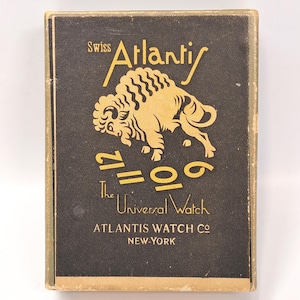 May include: A vintage watch box with a black background and gold lettering. The box features the words "Swiss Atlantis" above a gold illustration of a bison. Below the bison are the numbers "12, 6, 9" and the words "The Universal Watch".
