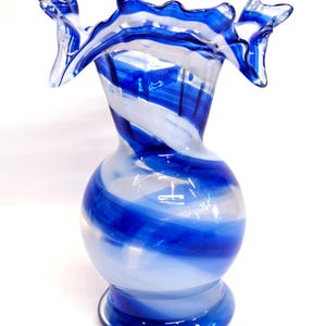 May include: A blue and white glass vase with a swirled design. The vase has a wide mouth and a rounded body.