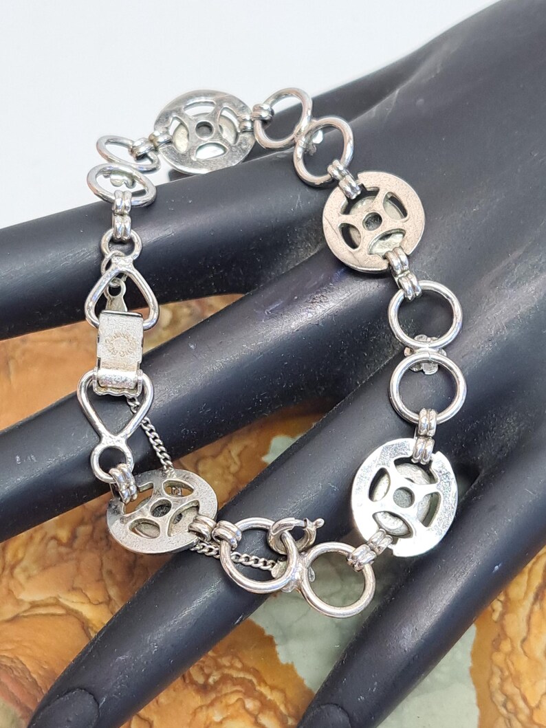 Op de afbeelding: Een zilveren armband met een kettinglinkontwerp en ronde bedels. De bedels hebben een uitgesneden patroon en zijn met kleine ringen aan de ketting bevestigd.