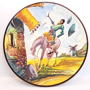 May include: A ceramic plate with a colorful illustration of a man on horseback riding through a field with a windmill in the background. The plate has a brown rim.