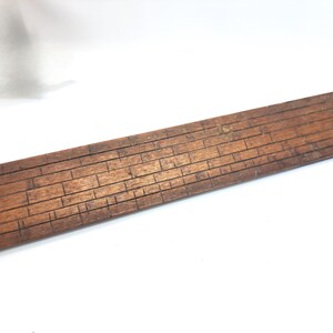 May include: A wooden ruler with a brick pattern. The ruler is brown and has a smooth surface.
