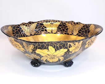 May include: A black and gold bowl with a floral and butterfly design. The bowl has a scalloped rim and three feet.