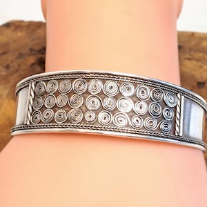 May include: Silver-toned cuff bracelet featuring a repeating spiral design. The bracelet has a wide band with a textured pattern of small, swirling spirals. The edges are detailed with a twisted rope design, and the ends are smooth.