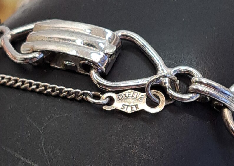 Op de afbeelding: Close-up van een zilveren kettinghalsband sluiting met een 'DIXIE STER' stempel. De ketting is gemaakt van kleine, met elkaar verbonden zilveren stukjes.