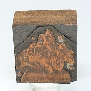 May include: A wooden printing block with a copper plate depicting a scene of three figures riding a horse. The figures are in relief and the horse is facing the right. The block is rectangular and has a dark brown finish.