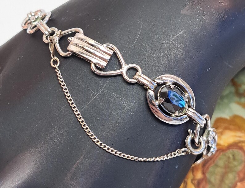 Op de afbeelding: Een zilveren armband met een blauwe strasssteen en een kettingdetail.