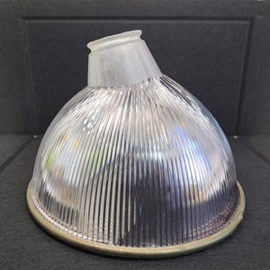 May include: A clear glass light fixture with vertical ridges and a frosted top. The fixture has a brass-colored base and is designed to direct light. The overall shape is a half-dome.