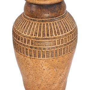 May include: A brown ceramic vase with a textured surface and a geometric design. The vase is signed "Zinnart".