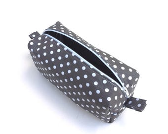 May include: A rectangular pencil case made of dark gray fabric featuring a white polka dot pattern. The case has a top zipper closure with a white zipper track and a small fabric loop attached to one end for easy handling and storage.