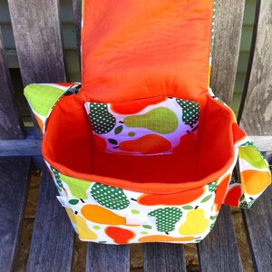 May include: A handmade fabric bag with a flap, featuring a vibrant pear pattern in orange, yellow, and green on a white background. The interior is bright orange, and a smaller pocket with a pear print is visible.