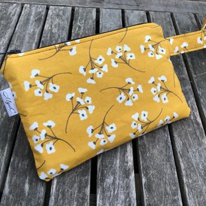 Puede incluir: Bolsa con cremallera de color amarillo mostaza con un estampado floral blanco y un asa peque&ntilde;a. La bolsa tiene una cremallera negra y una peque&ntilde;a etiqueta blanca con el texto "Alysa C".