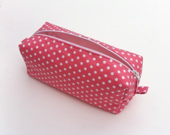 May include: A rectangular pencil case with a pink background and white polka dots. The case has a white zipper and a small fabric loop on the side. The interior is a light pink color.