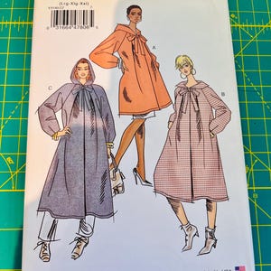 May include: A Very Easy Vogue sewing pattern envelope V9340 for sizes Lrg-Xlg-Xxl. The front displays three illustrations of long-sleeved coats with tie-neck closures, including a hooded version, a solid orange coat, and a plaid coat with a collar.
