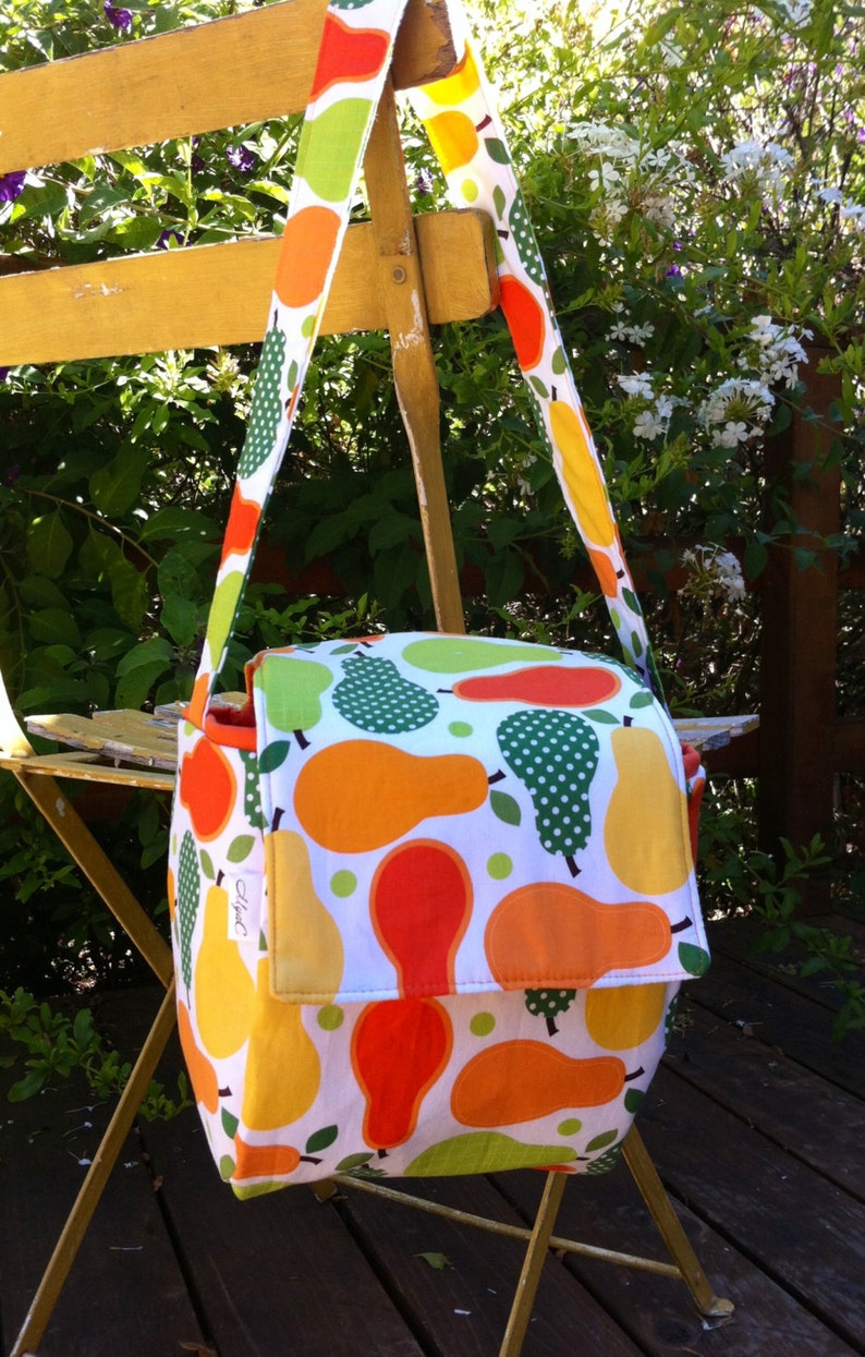 May include: A colorful shoulder bag with a white background and a pattern of orange, yellow, and green pears. The bag has a flap closure and a long strap. The bag is made of fabric.