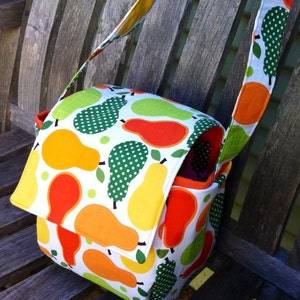 May include: A colorful crossbody bag with a flap closure, featuring a white background with a pattern of pears in shades of orange, yellow, and green. The bag has a matching strap and a red interior.