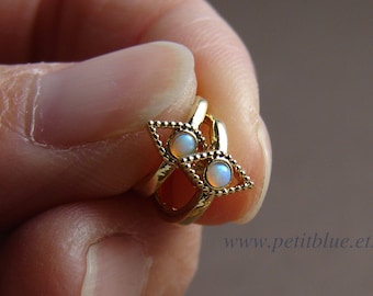 May include: Gold nose ring with two opal stones. The ring is in the shape of a triangle with a beaded edge.