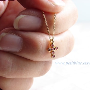 Op de afbeelding: Een gouden ketting met een klein kruisje als hanger. Het kruis is versierd met rode edelstenen.