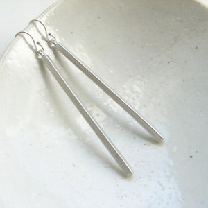 May include: A pair of silver bar earrings with a simple, minimalist design. The earrings are long and slender, with a smooth, polished finish.