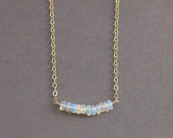 May include: A delicate gold chain necklace with a row of small, iridescent opal beads. The necklace is simple and elegant, perfect for everyday wear.