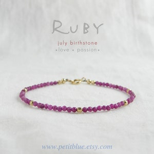 May include: A delicate bracelet made with small, faceted ruby beads and gold accents. The bracelet is a simple design and is perfect for everyday wear. The text "RUBY" is written in cursive at the top of the image. The text "july birthstone" is written below the word "RUBY". The text "*love* *passion*" is written below the text "july birthstone". The text "www.petitblue.etsy.com" is written at the bottom of the image.