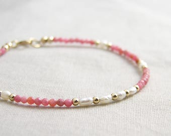 Puede incluir: Un brazalete delicado con cuentas rosas y blancas, intercaladas con cuentas doradas. El brazalete tiene un cierre de broche.