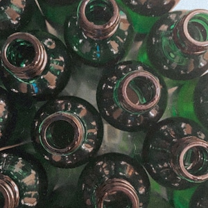 May include: A close-up of a group of green glass bottles with black lids. The bottles are arranged in a circular pattern and are all the same size and shape.
