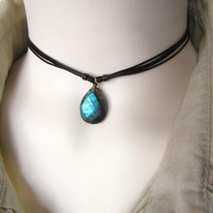 Peut inclure: Un collier ras du cou noir avec un pendentif en forme de goutte. Le pendentif est une pierre précieuse facettée aux teintes bleues et turquoise. Le collier est porté sur un mannequin.